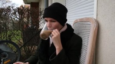 Kadın serin bir günde süpürge ve rahat kıyafetlerle dışarıda kahveden zevk alıyor..