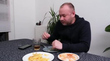 Ev ortamında balık ve patates kızartmasına odaklanmış bir adam yemeğin tadını çıkarıyor..