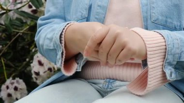 Mavi ceketli bir kadın, elleri birbirine kenetlenmiş bir bankta oturuyor. Sahne huzurlu ve sakin, kadının elleri bir sakinlik jesti ile birbirine kenetlenmiş.