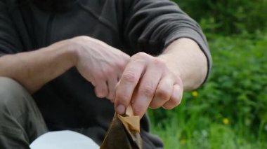 Bir adam çimenli bir alanda oturuyor ve elinde bir kağıt parçası tutuyor. Kağıt bir makbuz ya da bir not gibi görünüyor. Adamın keyfi yerinde ve rahat görünüyor.