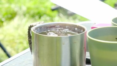 Bir fincan kahve diğer iki fincanın yanında bir masada oturuyor. Sahne açık havada ve bardaklar dışarıda bir masada.