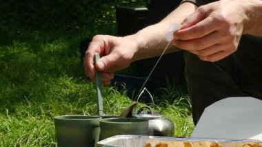 Bir adam çimlerin üzerinde oturuyor ve bir parça ip tutuyor. Uzakta bir şeye bakıyor.