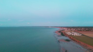 Hava sahili manzarası, temiz gökyüzü altında geniş kıyı şeridi ve sakin sular olduğunu gösteriyor..