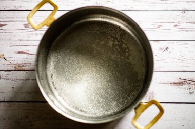 Beyaz ahşap yüzeyde pirinç saplı boş metal tencere..