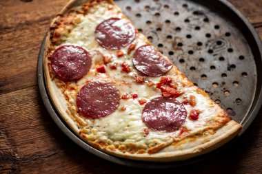 Kırsal ahşap masada yarısı yenmiş pepperoni pizzası..
