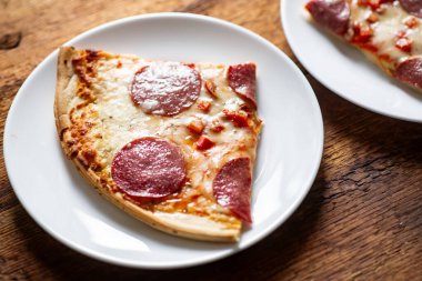 Beyaz tabakta, ahşap masa arkaplanlı bir dilim pepperoni pizza..