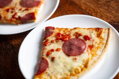 Biberli pizza dilimlerinin yakın planında beyaz tabaklar üzerinde ahşap masanın üzerinde.