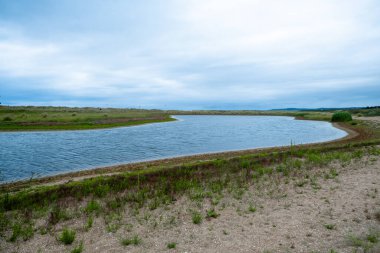 Açık kırsalda bulutlu gökyüzünün altında nehir kıvrımlı sakin bir manzara..