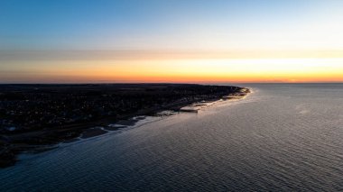 Sakin okyanus ve ufukta kıyı günbatımı manzarası.