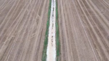 Geniş tarım arazisini kesen dar yolun havadan görünüşü.