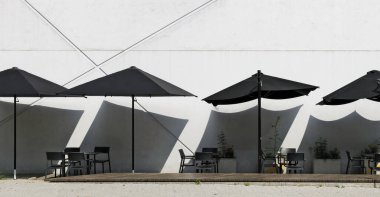 Beyaz duvarın yanında siyah şemsiyeli boş bir sokak kafesi.