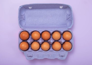 Mor üzerine mor tepside çiğ kahverengi organik yumurta. Üst görünüm.