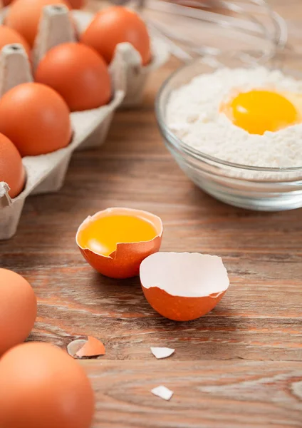 Bowl plate with flour and egg yolk with fresh raw eggs and metal whisk on wooden table