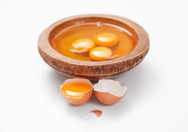 Three egg yolks in wooden plate on white table background with shell