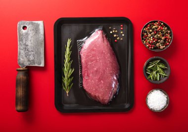Fresh raw sirloin fillet steak with meat cleaver and rosemary,salt and pepper on red background.Top view.
