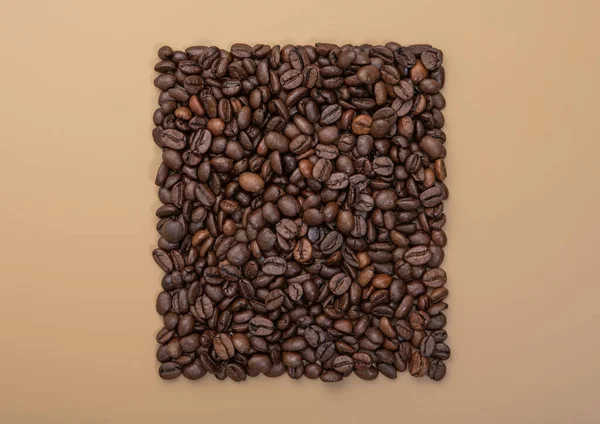Square of fresh raw coffee beans on beige background.Top view.