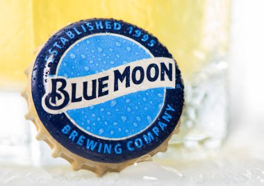 LONDON, UK - DECEMBER 15, 2022: Blue Moon wheat beer bottle cap with dew on white  with glass.