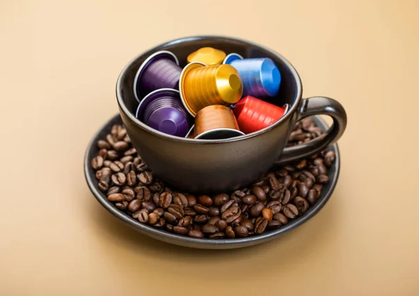 Cup with aluminium coffee capsules pods with fresh aroma coffee on beige background with raw coffee beans.