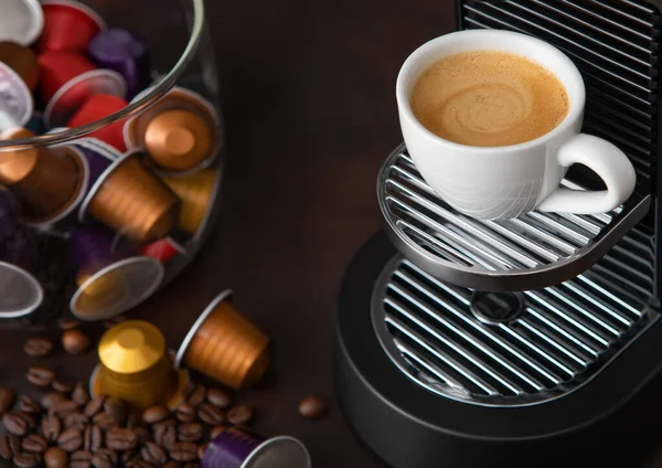 Coffee machine pods capsules with cup and raw aroma coffee beans on brown.