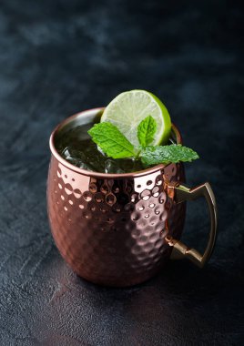 Moscow mule cocktail in a copper mug with lime and mint on dark kitchen table background