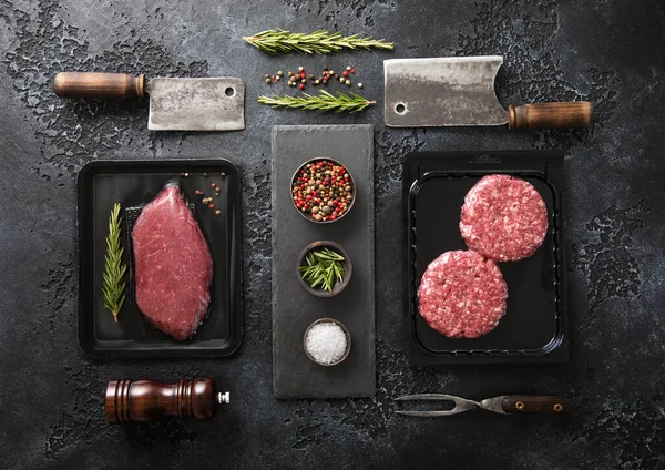 新鲜的生牛肉片牛排和肉馅汉堡包放在真空盘子里 配上切碎和迷迭香 黑色背景 配迷迭香 — 图库照片