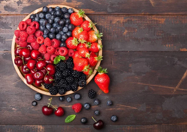 新鮮な有機夏の果実は 濃い木製のテーブルの背景に丸い木製のトレイに混合します ラズベリー イチゴ ブルーベリー ブラックベリー チェリー トップ表示 — ストック写真