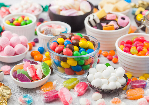 Молочные шоколадные конфеты woth оболочка в банке с различными желе десен конфеты на белом столе с лакрицей всех сортов и клубничные конфеты с различными кислыми сахарными деснами.