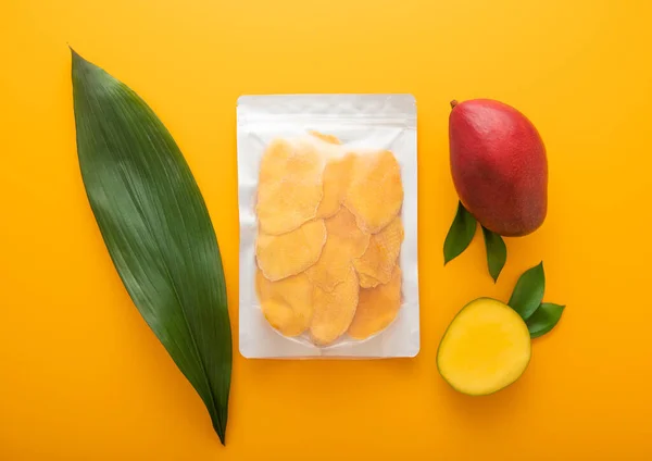 Stock image Large pack of dried mango slices with leaf and raw mango on yellow background.Top view.