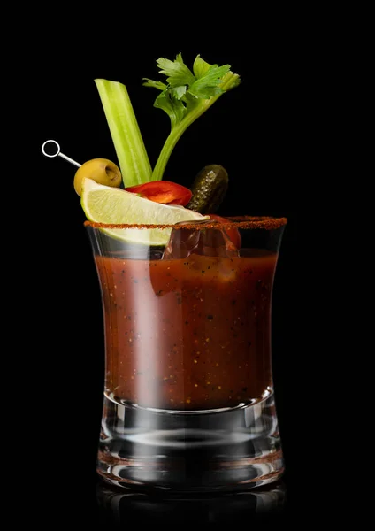 Bloody mary with cocktail stick and pepper and olive, celery piece and lime slice on black.