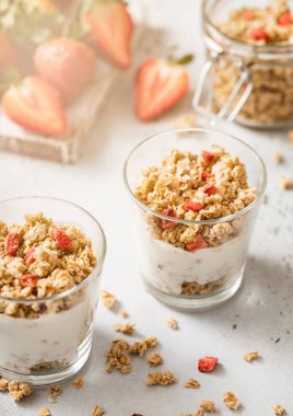 İki granola ve yoğurt porsiyonlu taze çilek ve güneş ışığı..