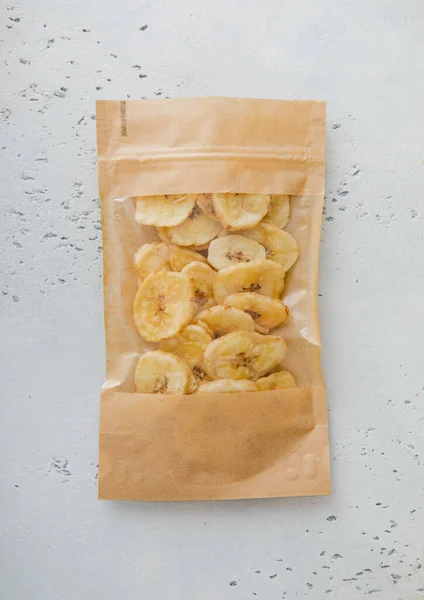 Pack of dried healthy banana chips on light board.