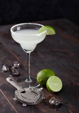 Klasik bir bardak limonlu Margarita kokteyli ve ahşap masa arkasında buz küplü süzgeç..