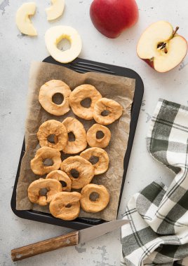 Pişirme tepsisinde bıçak ve mutfak havlusuyla kurutulmuş elma halkaları..