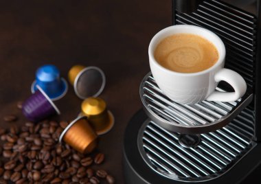 Espresso makinesinden alınmış sıcak aromalı kahve bardağı koyu arkaplan ve çiğ fasulye.