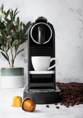 Beyaz fincanlı espresso kahve makinesi ve kapsüller hafif mutfakta çiğ fasulye aromalı.