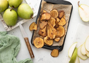 Kurumuş armut dilimleri fırın tepsisinde yeşil olgun armutlar ve açık arkaplanda bıçak..