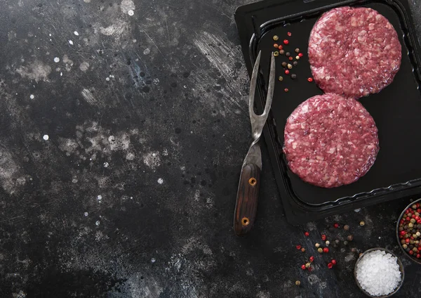 在黑暗的厨房背景下 用叉子和胡椒密封在真空盘子里的生牛肉汉堡包 — 图库照片