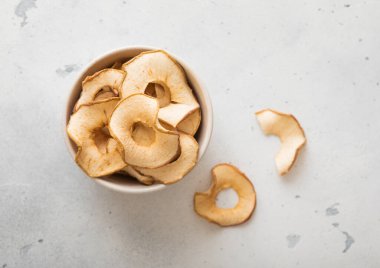 Açık arkaplan üzerinde kurumuş elma halkaları olan kasenin üst görüntüsü.