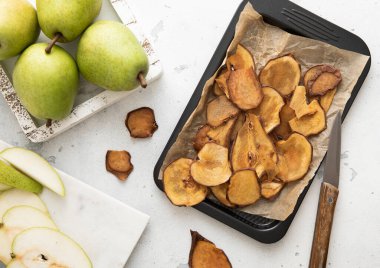 Kurumuş armut dilimleri fırın tepsisinde yeşil olgun armutlar ve açık arkaplanda bıçak..