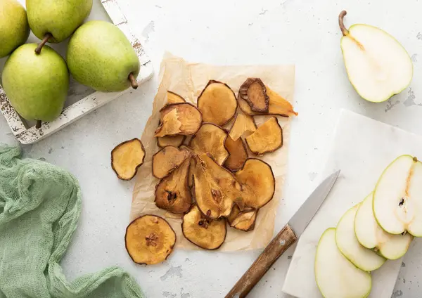 Kurumuş armut dilimleri kabartma kağıdının üzerinde yeşil olgun armutlar ve ışık masasında cips dilimleri..