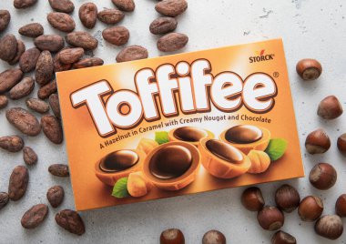 LONDON, UK - MARCH 02, 2024: Box of Toffifee chocolate and caramel candies with raw hazelnuts and cocoa beans on light background. clipart
