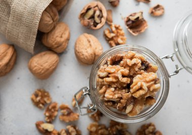 Cam kavanozda ceviz kabuğu soyulmuş ve arka planda fındık dolu keten poşet..