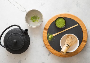 Japon demir çaydanlığı ile kibrit tozu yeşil çay tozu çırpı ve kaşık ve kase ile beyaz arka planda süzgeç.
