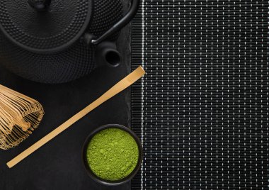 Bambu kaşıklı yeşil kibrit çayı ve siyah arka planda Japon demir çaydanlığı..