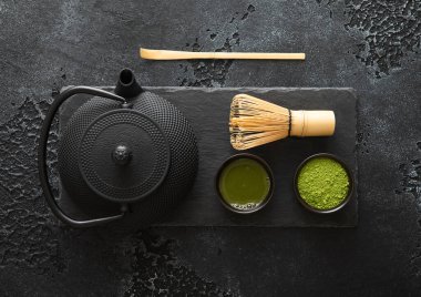 Organik kibrit yeşil çay tozu bambu çırpı ve kaşık ve Japon geleneksel demir çaydanlığı ile siyah arka planda..