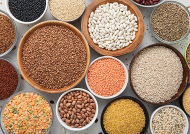 Çeşitli sağlıklı mısır gevrekleri olan kâselerin üst görüntüsü. Bulgur, fasulye, kinoa, bezelye, kuskus ve açık mutfak arka planında nohut ve karabuğday tohumu olan kenevir..