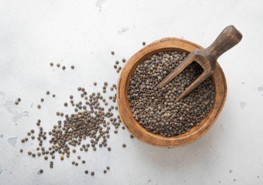 Çiğ siyah mercimek tohumları ahşap kasede ve ışık masasında kepçeyle..