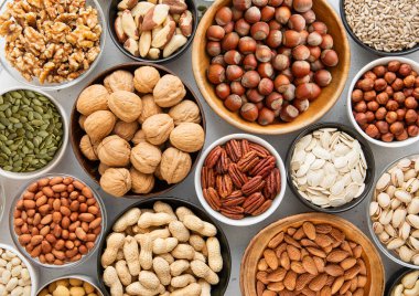 Fıstık, fındık, ceviz, badem, fıstık, fıstık, ayçiçeği, balkabağı, chia, ceviz ve fındık karışımı sağlıklı fındık ve tohumlar mutfak masasında çeşitli kaselerde..