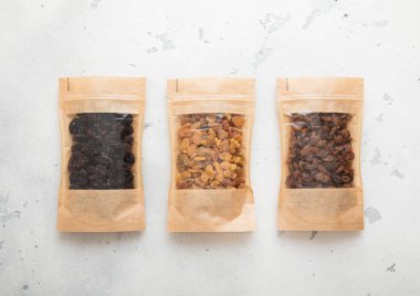 Açık arkaplanda organik yeşil ve kahverengi kuru üzümlü paketler..