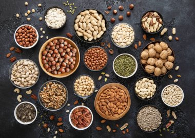 Çeşit çeşit çiğ, sağlıklı fındık ve tohumlar çeşitli kaselerde siyah mutfak zemininde. Fıstık, fındık, ceviz, badem, fıstık, ayçiçeği, balkabağı, chia ve kaju..